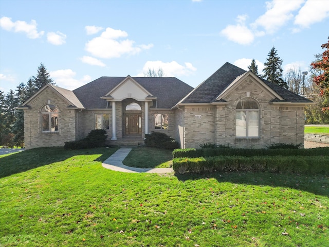 view of front facade with a front yard, brick siding, and a shingled roof