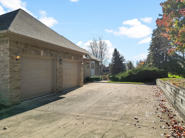 view of side of home with a garage, brick siding, driveway, and roof with shingles