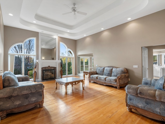 living area with a ceiling fan, a tray ceiling, a high ceiling, light wood-style flooring, and a fireplace