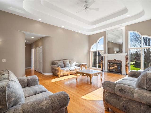 living room featuring a tray ceiling, wood finished floors, a fireplace, and ceiling fan