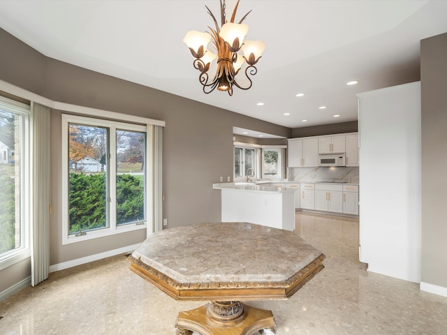 kitchen with baseboards, white microwave, white cabinets, and light countertops