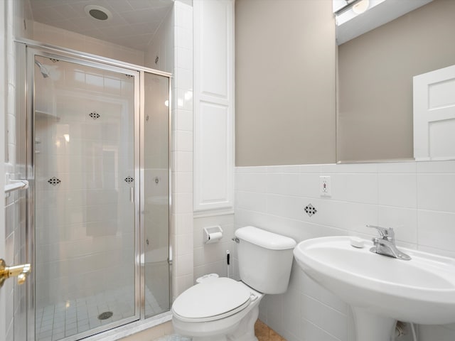 bathroom featuring toilet, wainscoting, a stall shower, tile walls, and a sink