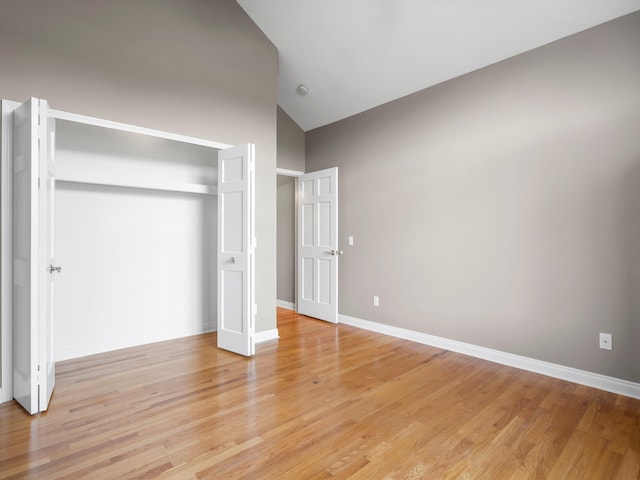 unfurnished bedroom featuring a closet, baseboards, light wood-type flooring, and lofted ceiling