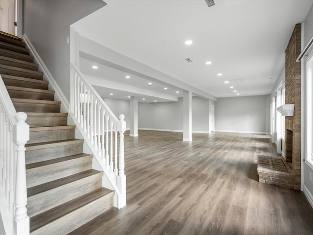 basement featuring stairs, a brick fireplace, recessed lighting, and wood finished floors