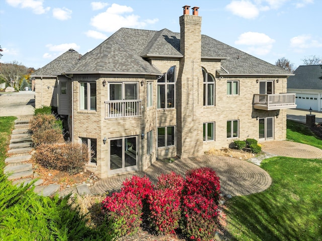 rear view of property with brick siding, a shingled roof, a chimney, a yard, and a balcony