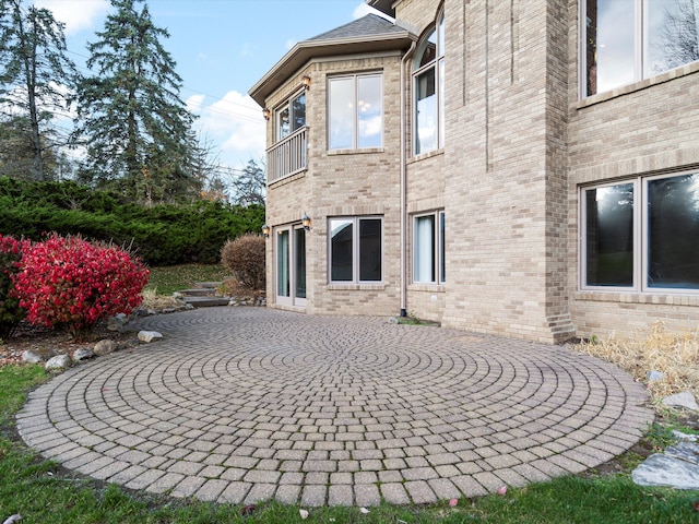 rear view of house with brick siding, a patio area, and a balcony