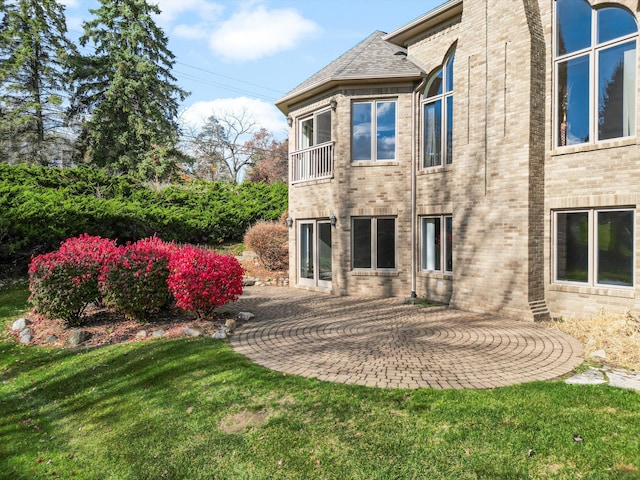 rear view of house featuring brick siding, a patio area, a yard, and a balcony