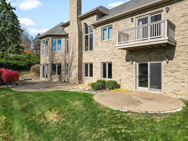 rear view of house with brick siding, a lawn, a chimney, a balcony, and a patio