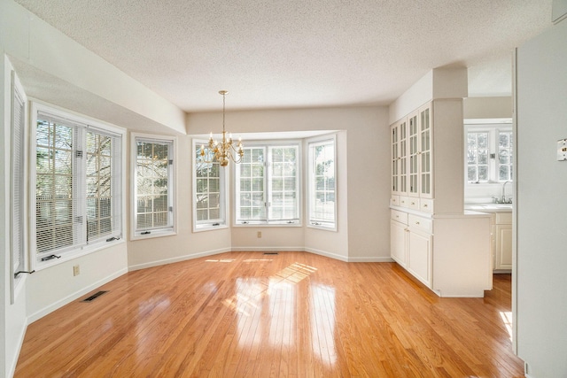 unfurnished dining area with visible vents, a healthy amount of sunlight, and light wood finished floors