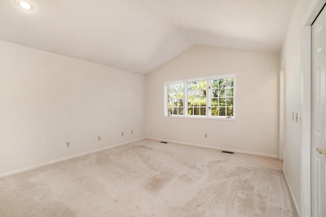 empty room featuring visible vents, light carpet, baseboards, and vaulted ceiling