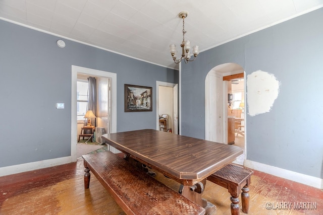 dining area featuring baseboards, arched walkways, wood-type flooring, crown molding, and a chandelier