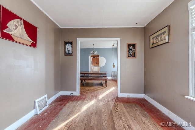 hall with ornamental molding, wood finished floors, visible vents, and baseboards