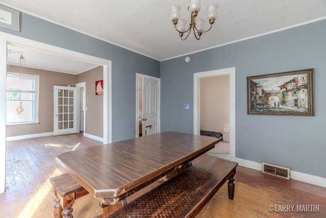 dining room featuring hardwood / wood-style floors, baseboards, visible vents, ornamental molding, and a notable chandelier