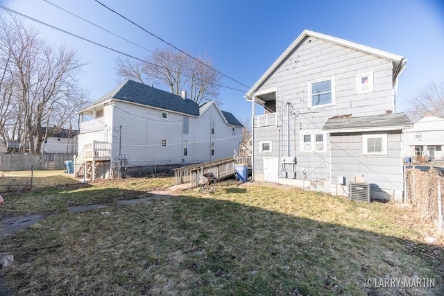 rear view of property with central AC unit, a lawn, and fence