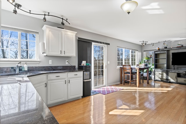 kitchen featuring white cabinetry, dark stone countertops, light wood-style flooring, and a sink