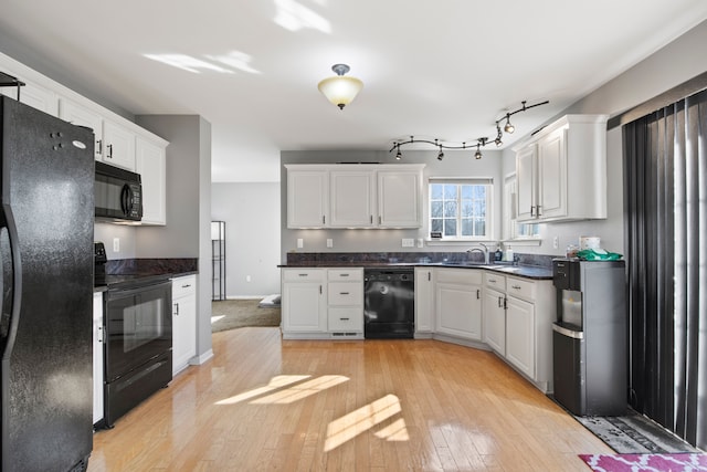 kitchen featuring black appliances, a sink, dark countertops, white cabinetry, and light wood finished floors