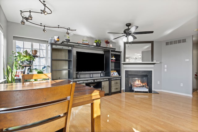 living area with visible vents, baseboards, wood finished floors, a glass covered fireplace, and a ceiling fan