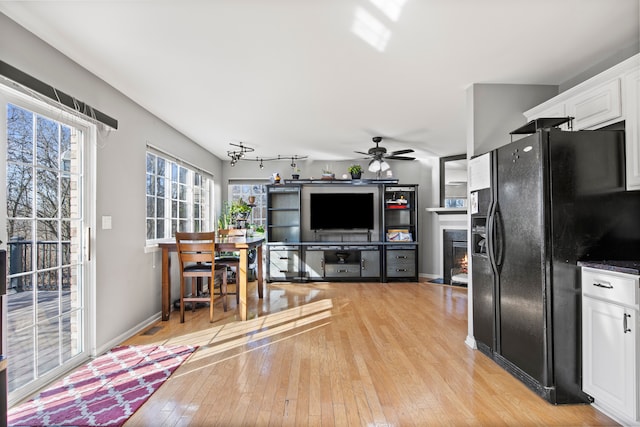 kitchen with a fireplace with flush hearth, a ceiling fan, black fridge, white cabinetry, and light wood-style floors