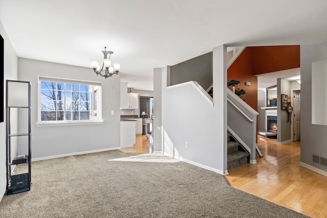 living area featuring light carpet, a notable chandelier, a glass covered fireplace, stairway, and baseboards