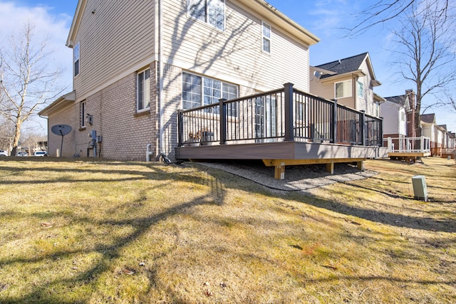 back of property with brick siding, a wooden deck, and a yard