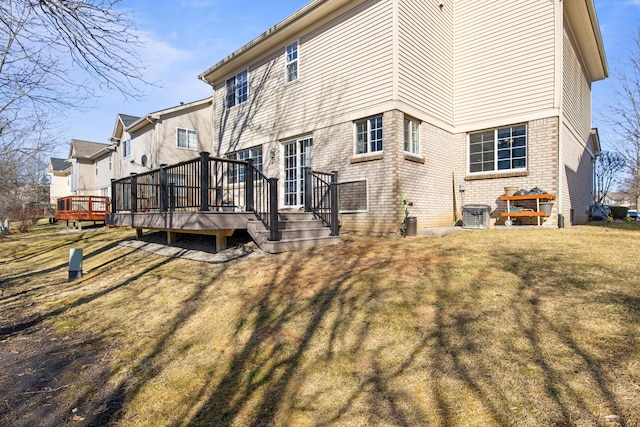 back of house with brick siding, central AC unit, a lawn, and a deck