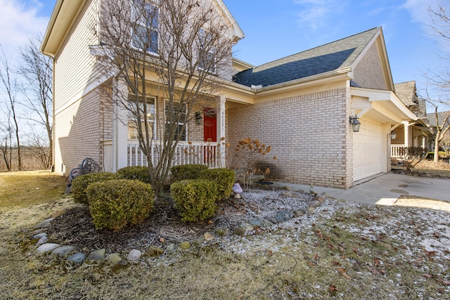 traditional home featuring driveway, an attached garage, covered porch, a shingled roof, and brick siding