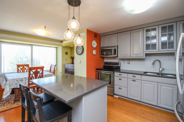 kitchen featuring dark countertops, light wood-type flooring, gray cabinets, stainless steel appliances, and a sink