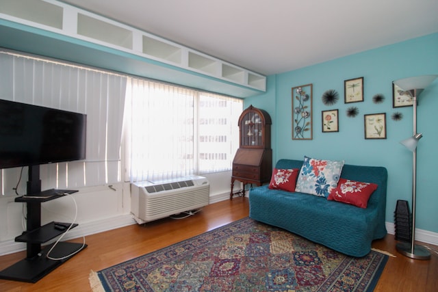 living area with baseboards, a wall unit AC, and wood finished floors