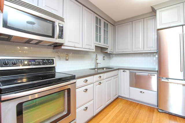 kitchen featuring light wood-type flooring, decorative backsplash, appliances with stainless steel finishes, a warming drawer, and a sink