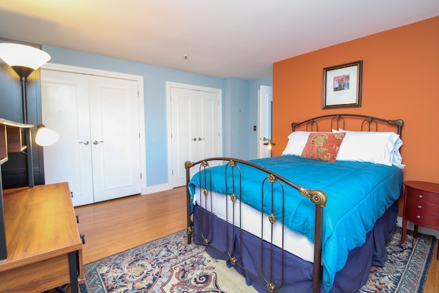 bedroom featuring two closets, baseboards, and wood finished floors