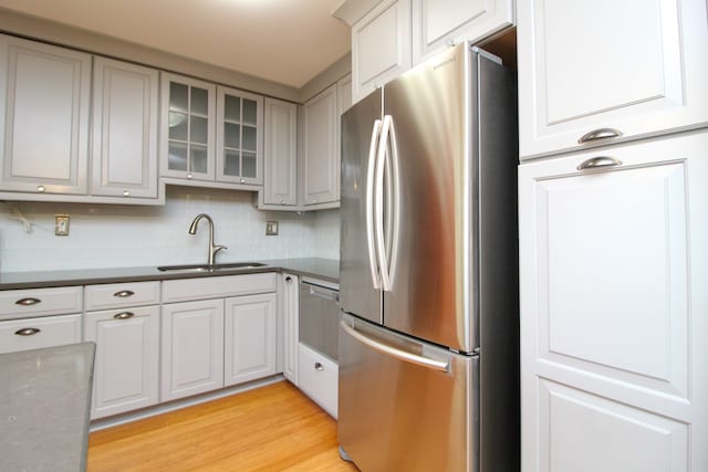 kitchen featuring freestanding refrigerator, a sink, glass insert cabinets, dark countertops, and light wood-type flooring