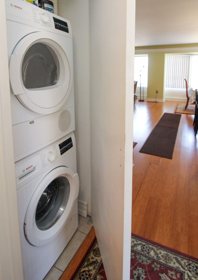 washroom with baseboards, stacked washer and dryer, wood finished floors, and laundry area