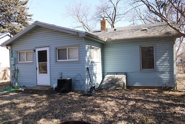 rear view of property featuring central AC unit, roof with shingles, and a chimney