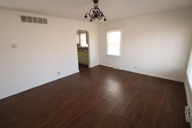 empty room with visible vents, dark wood-type flooring, arched walkways, baseboards, and a chandelier