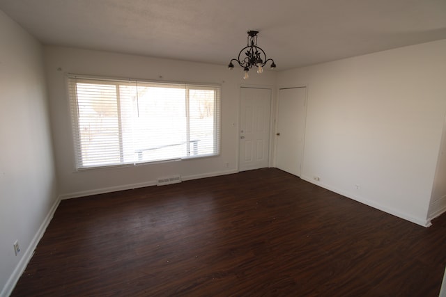 empty room featuring dark wood finished floors, a notable chandelier, baseboards, and visible vents