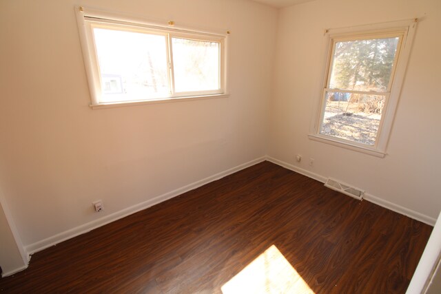 empty room featuring a healthy amount of sunlight, visible vents, dark wood-style flooring, and baseboards