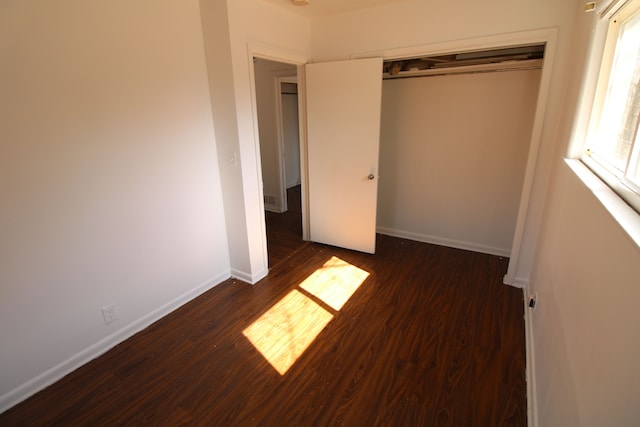 unfurnished bedroom featuring a closet, dark wood-type flooring, and baseboards