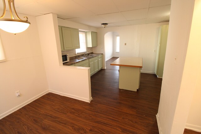 kitchen with white microwave, dark wood finished floors, arched walkways, and a sink