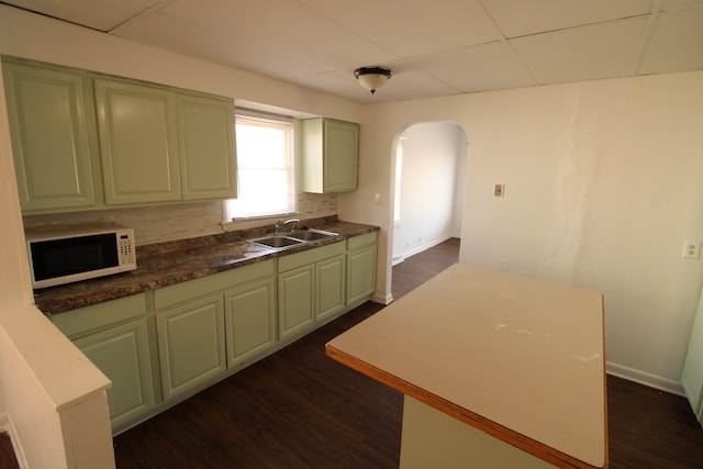 kitchen featuring white microwave, tasteful backsplash, a sink, arched walkways, and dark wood-style flooring