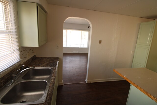 kitchen featuring a sink, dark countertops, dark wood-style floors, arched walkways, and baseboards