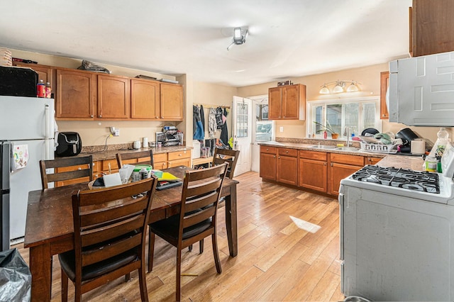 kitchen with light wood finished floors, a sink, white appliances, brown cabinetry, and light countertops