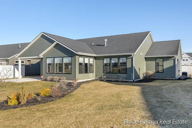 view of front of house featuring cooling unit, roof with shingles, a front yard, and fence