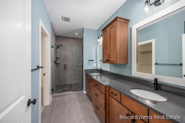 bathroom with visible vents, double vanity, a stall shower, a sink, and tile patterned floors