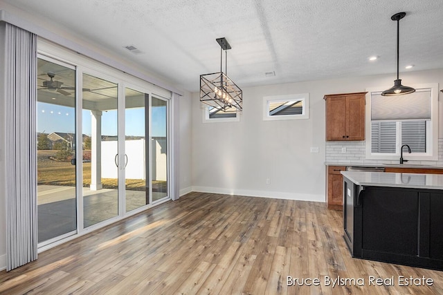 kitchen featuring light wood-type flooring, visible vents, backsplash, brown cabinetry, and light countertops