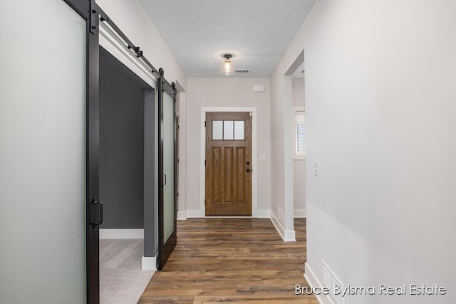 entryway with a barn door, baseboards, visible vents, and wood finished floors