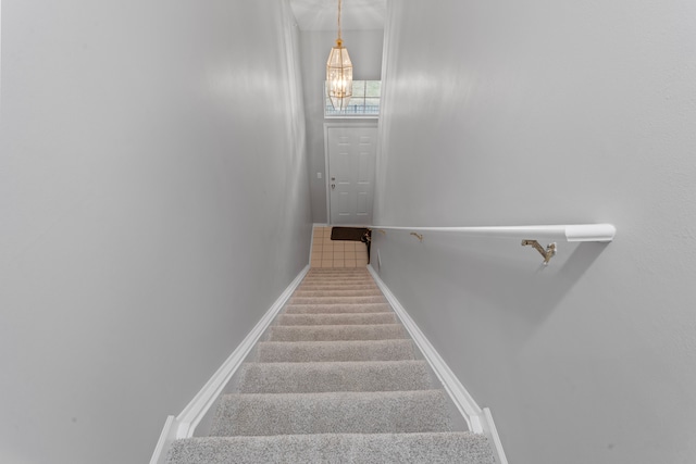 staircase featuring a notable chandelier, baseboards, and carpet