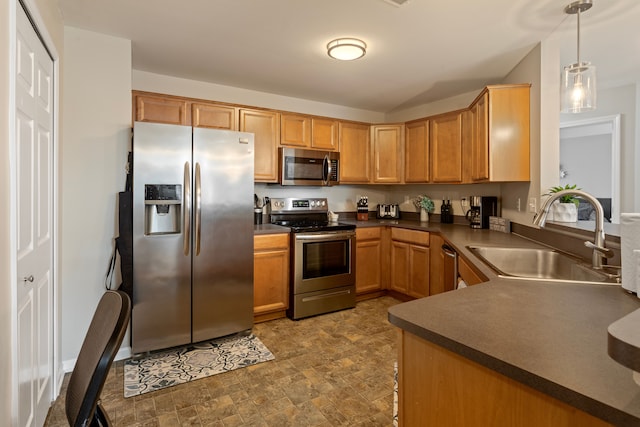 kitchen featuring stone finish floor, a sink, decorative light fixtures, dark countertops, and stainless steel appliances