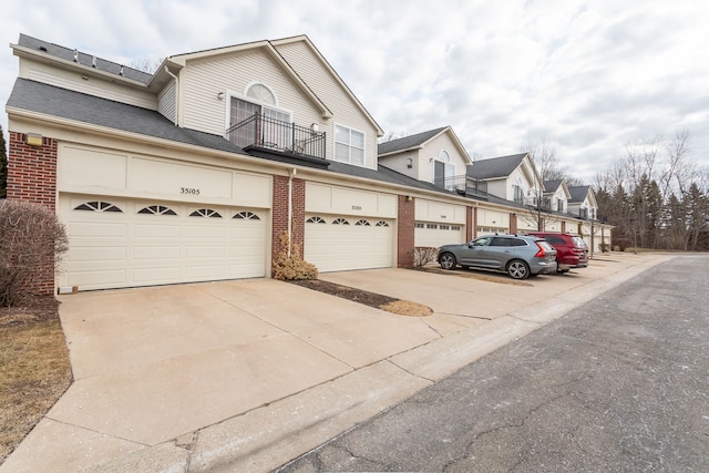 townhome / multi-family property featuring a garage, brick siding, concrete driveway, and a balcony