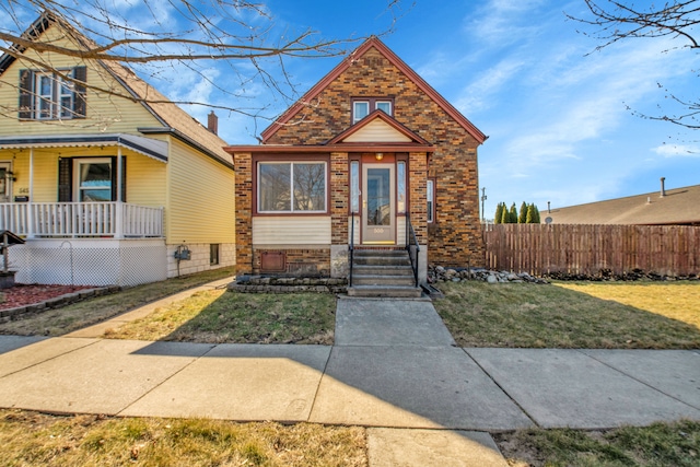 view of front of property with a front yard, a porch, fence, and brick siding