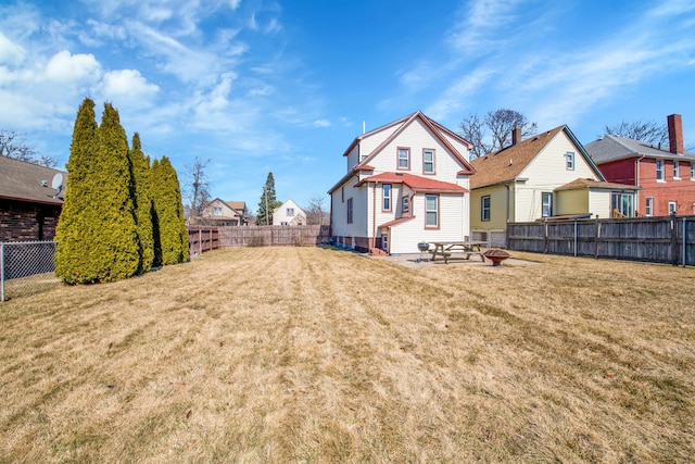 rear view of house with a fenced backyard, a lawn, and a fire pit